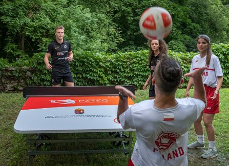 fotografia. dni wyszehradzkie w willi decjusza. mecz teqball na wolnym powietrzu. czworo zawodników wokół stołu ustawionego na trawie. w tle budynek willi decjusza.